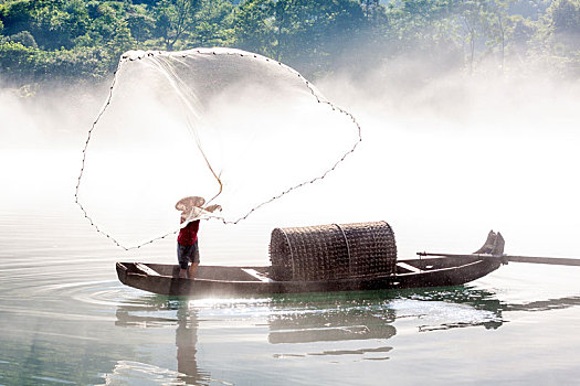 渔夫在飘渺晨雾的湖泊中打鱼
