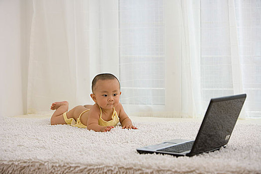 趴在地毯上玩电脑的婴儿