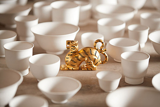 金色的老虎摆件以白色茶碗为环境在浅色实木桌面上