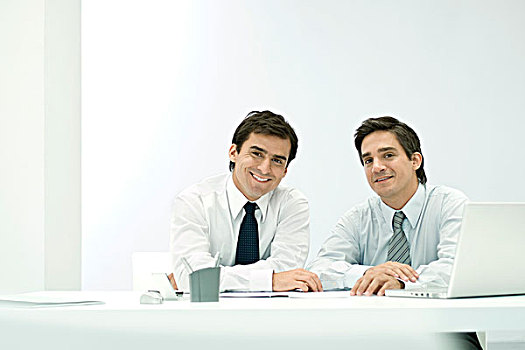 男性,合作伙伴,坐,并排,书桌,看镜头,微笑