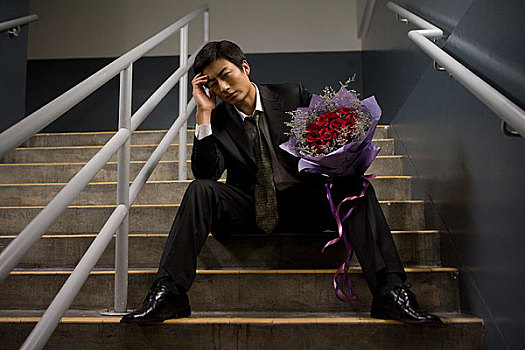 坐在建筑台阶上手捧鲜花等人的男士