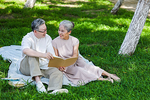 幸福的老年夫妇坐在公园草地上看书