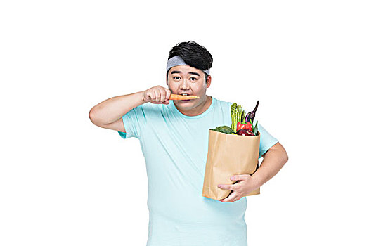 肥胖的年轻男子拿着各种蔬菜在吃胡萝卜