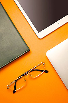 书,鼠标,电脑等办公用品陈列在橙色背景的桌面上