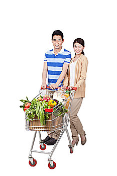一对青年男女合推一辆装满蔬菜的购物车