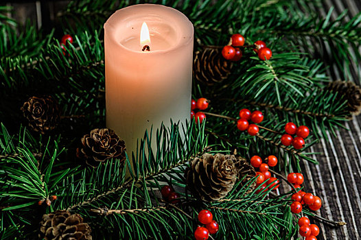 摆放在木质桌面上的圣诞树,红浆果和燃烧中的白色蜡烛