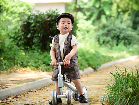 阳光下林荫小路上穿着短袖西服扶着滑滑车开心的小男孩