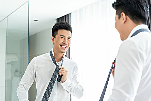 年轻男子在镜子前系领带