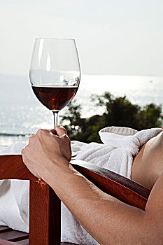 年轻男人在游泳池边休息喝红酒