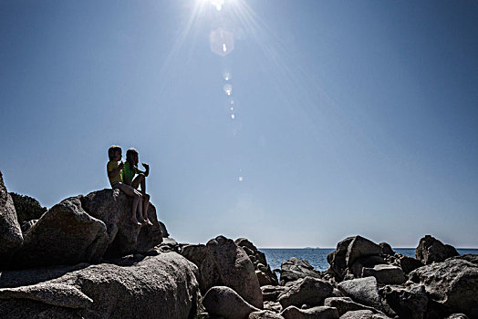 两个女孩,坐,石头,海洋,逆光