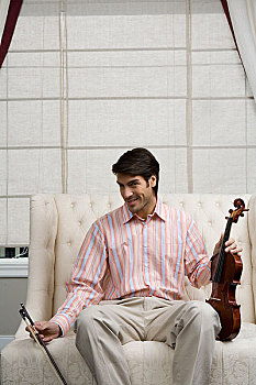 一位先生拿着小提琴坐在沙发上