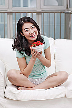 年轻女士坐在沙发上拿着一碗草莓