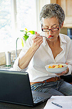女人吃水果沙拉,使用笔记本电脑