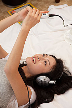 年轻女人躺在床上戴耳机听音乐