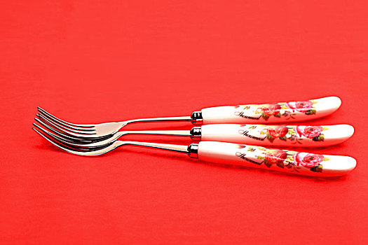 三把银色带红色花纹的叉子摞在一起