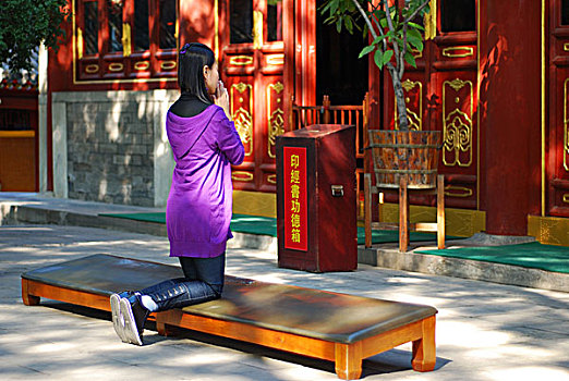 一名年轻女性跪在寺庙中祈祷