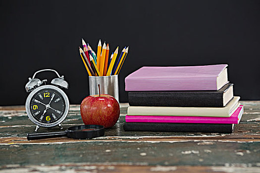 一堆,书本,闹钟,苹果,放大镜,笔,固定器具,木桌子