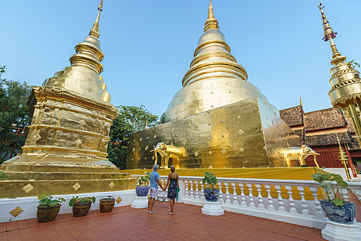 一对情侣在泰国清迈老城里的著名寺庙帕辛寺中旅行,牵手欣赏高大的金色佛塔
