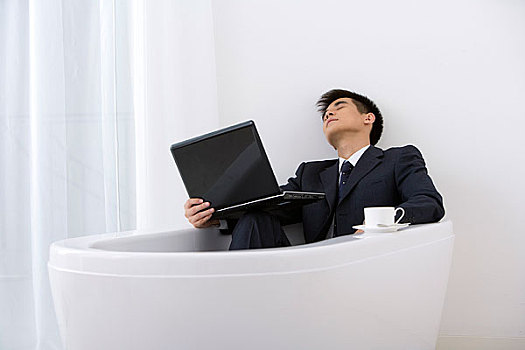 一个穿职业装的男人拿着电脑在浴缸里