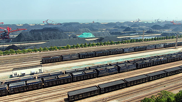 山东省日照市,蓝天下的港口煤炭堆场整齐划一,火车满载货物铿锵前行