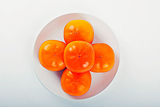 一个白色的盘子里盛着柿子