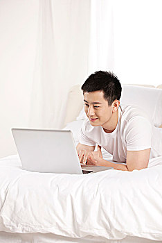 躺在床上玩电脑的青年男性