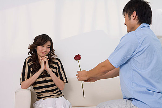 一个男人拿着一支花向坐在沙发上的女人求婚
