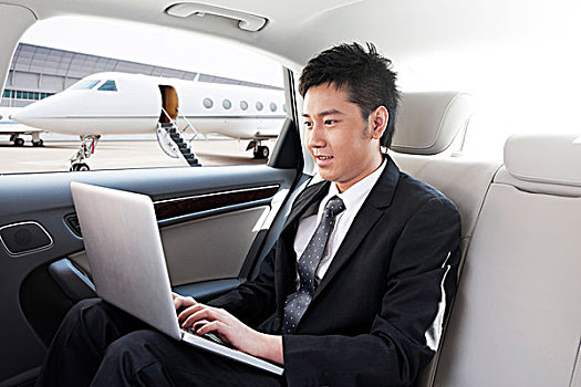 商务男士坐在轿车里使用笔记本电脑