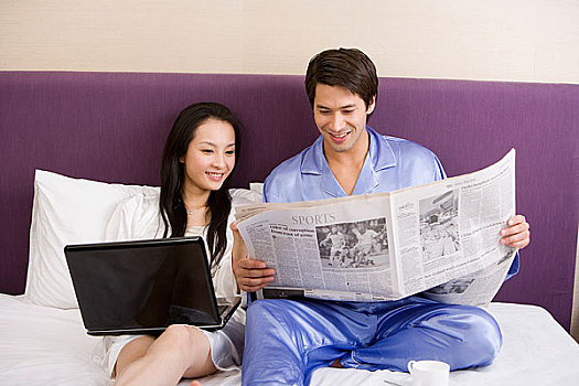 一对年轻的夫妻在床上看报玩电脑