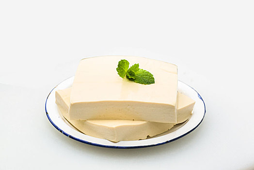 两块豆腐盛在盘子里,绿色薄荷叶点缀,放在白色背景上
