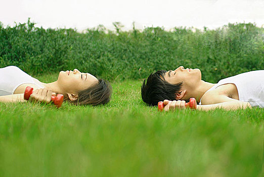 手握哑铃闭着眼睛躺在草地上的年轻男女