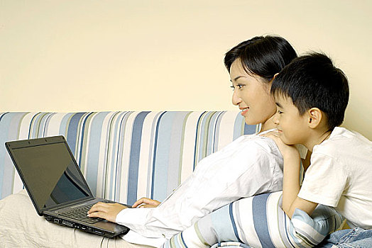 靠在沙发上使用电脑的年轻女人和抱着她的儿子