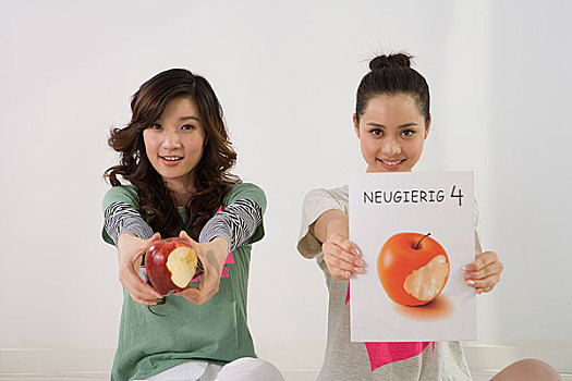 对着镜头举着苹果和书的两个女人