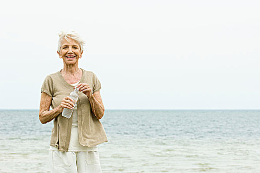 老年,女人,站立,海滩,拿着,水瓶,看镜头,微笑