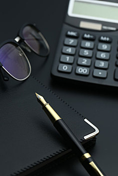 金笔,计算器,眼镜和笔记本放在黑色桌面上