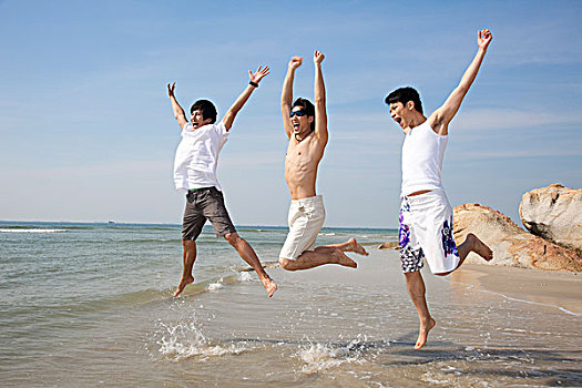 三个休闲装年轻男人在海边跳跃