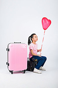 坐在行李箱上手拿气球的小女孩
