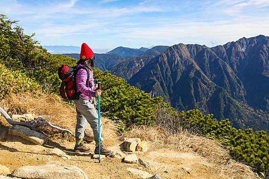 一个手拿登山杖站在山顶看着远方风景的女性徒步旅行者全身背影
