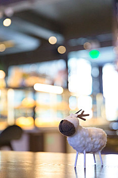 一只羊毛毡制作成的小鹿摆件摆放在咖啡馆的木桌上