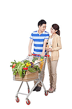 一对青年男女手拿面包和一辆装满蔬菜的购物车