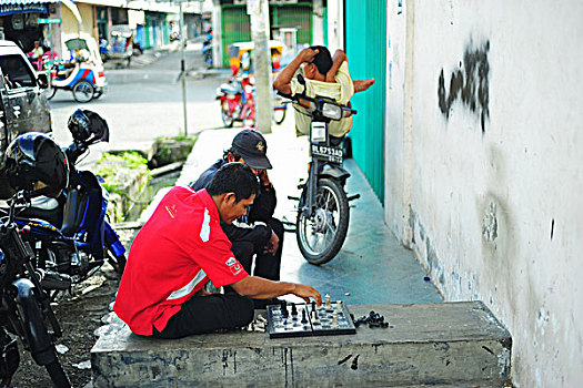 indonesia,sumatra,banda,aceh,2,men,playing,chess,while,the,other,is,resting,on,motocycle