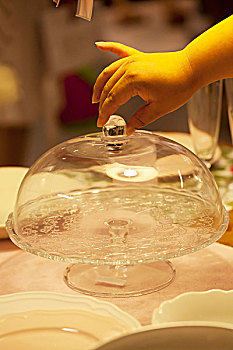一只手正在打开一个透明的果盘上面的透明玻璃罩
