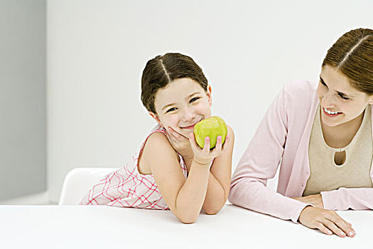 小女孩,坐,桌子,母亲,手,下巴,拿着,苹果,看镜头,微笑