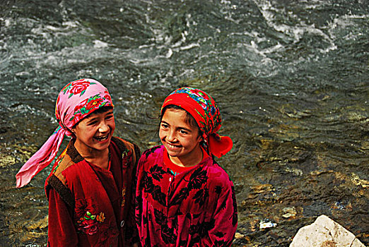tajikistan,penjakent,two,girls,in,colorful,traditional,dress,smiling,by,the,river