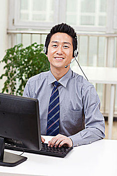 一个在办公室用电脑戴耳机的青年商务男士