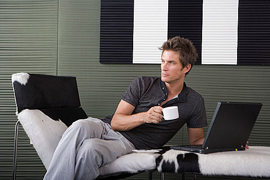 一位先生坐在躺椅上喝咖啡玩电脑