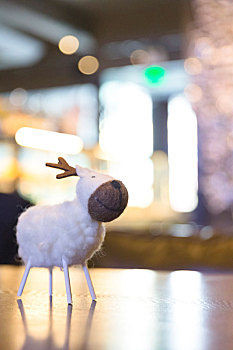 一只羊毛毡制作成的小鹿摆件摆放在咖啡馆的木桌上