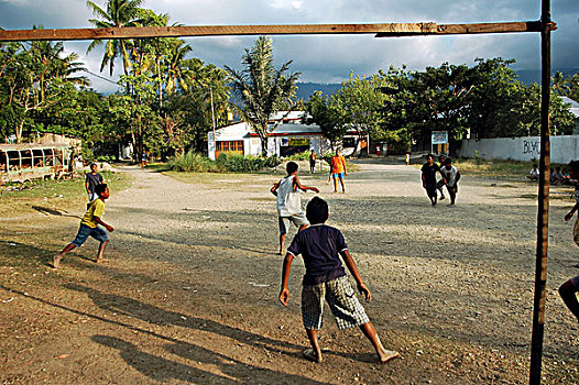 east-timor,timor-leste,dili,group,of,asian,children,playing,soccer,in,the,street,under,dark,grey,clouds