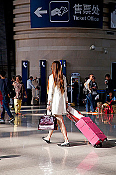 北京南站候车穿着白色外套拉着粉色拉杆箱的长发美女