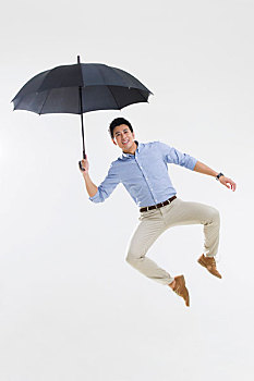 快乐的年轻男子打着雨伞跳跃